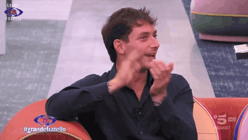 a man sitting on a couch with the words grandefratello on the bottom right