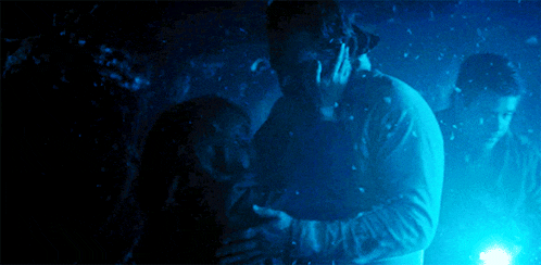 a man and a woman are hugging in a dark room with blue lights behind them