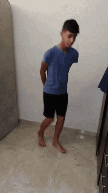 a boy in a blue shirt and black shorts is standing on a tile floor