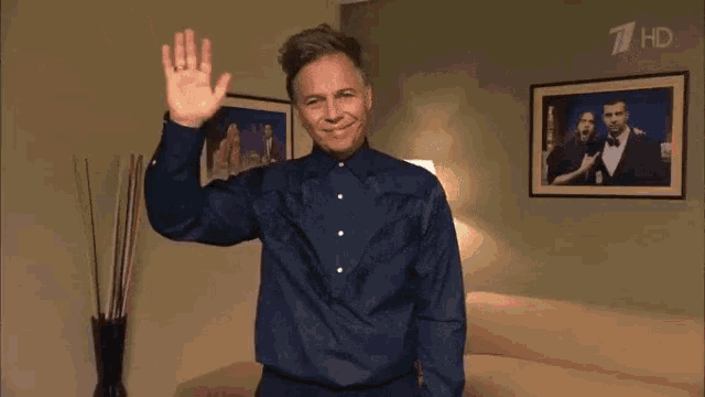 a man in a blue shirt is waving in front of a picture of a man in a suit