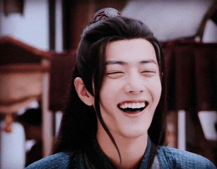 a young man with long hair is laughing with his eyes closed and his mouth open .