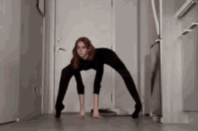 a woman in a black bodysuit is doing a split on the floor .