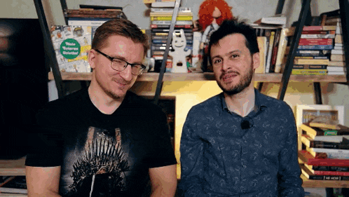 two men are sitting next to each other in front of a bookshelf and one of them has a t-shirt that says thrones