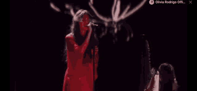 a woman in a red dress is singing into a microphone on a stage with a harp in the background .