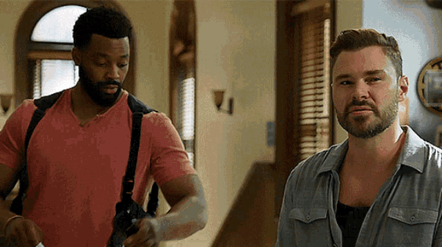 two men are standing next to each other and one has a gun on his back