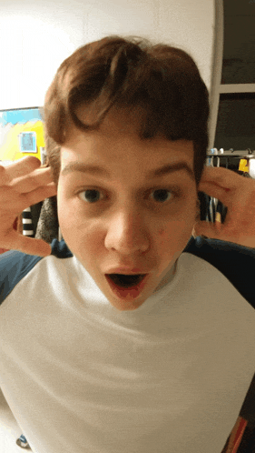 a young boy making a funny face with his hands over his ears