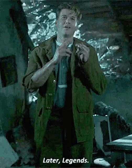 a man in a green jacket is standing in a room with a cigarette in his hand and a cigarette in his mouth .
