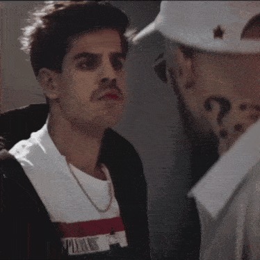 a man wearing a shirt that says pleasures is looking at another man
