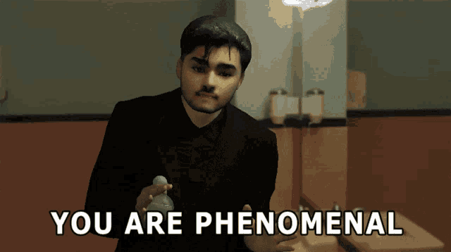 a man in a black suit is standing in a bathroom with the words " you are phenomenal " above him