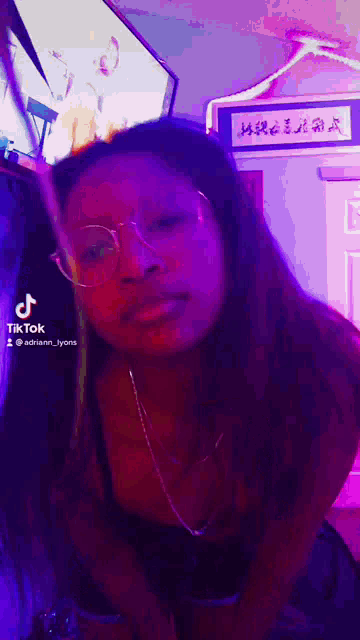 a woman wearing glasses is standing in a room with purple lights .