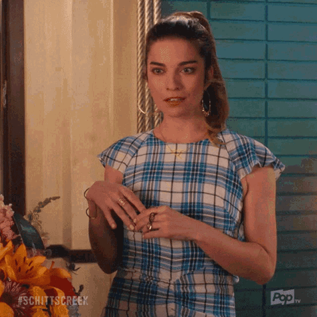 a woman wearing a blue and white plaid shirt is standing in front of flowers and a pop tv sign
