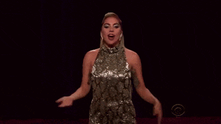 a woman in a sequined dress is singing on a stage with her arms outstretched .