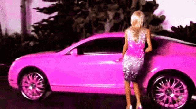 a woman is standing next to a bright pink car