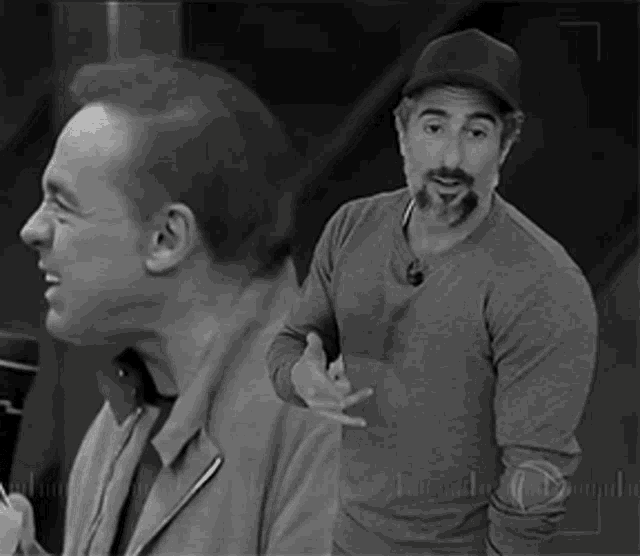 two men are standing next to each other and one is wearing a hat .