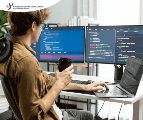 a man sits at a desk with two computer monitors and a laptop with the words impressico business solutions on the bottom left