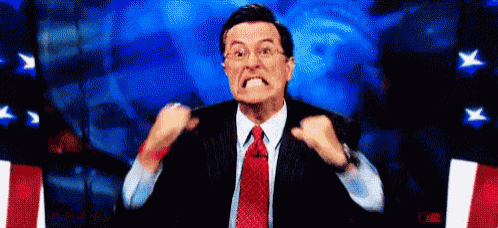 a man in a suit and tie is making a funny face while holding his fists up in the air .