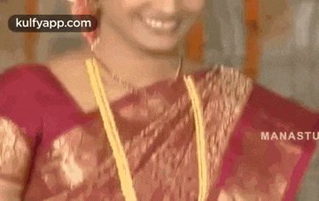 a close up of a woman wearing a red saree and gold necklace .
