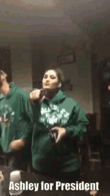 a woman in a green sweatshirt is dancing with a man in a green hoodie .