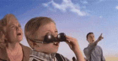a boy wearing sunglasses is looking through binoculars while a woman cries .
