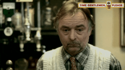 a man in a plaid shirt and tie is standing in front of a sign that says time gentlemen please
