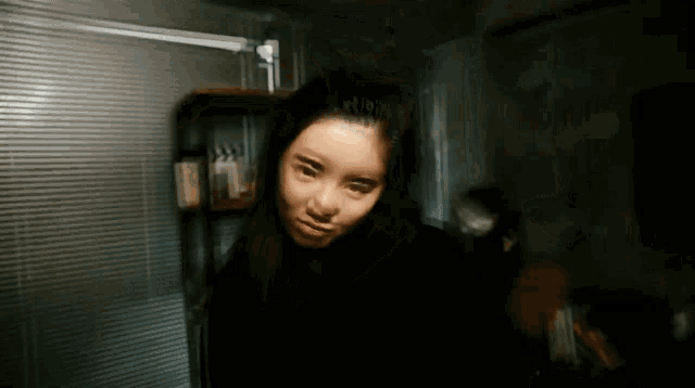 a blurry photo of a woman in a dark room with blinds
