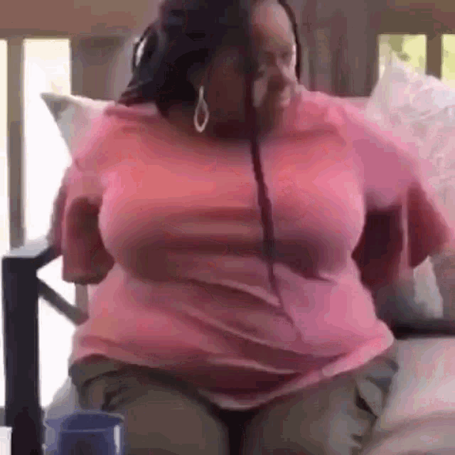 a woman is sitting on a bed wearing a pink shirt and earrings .