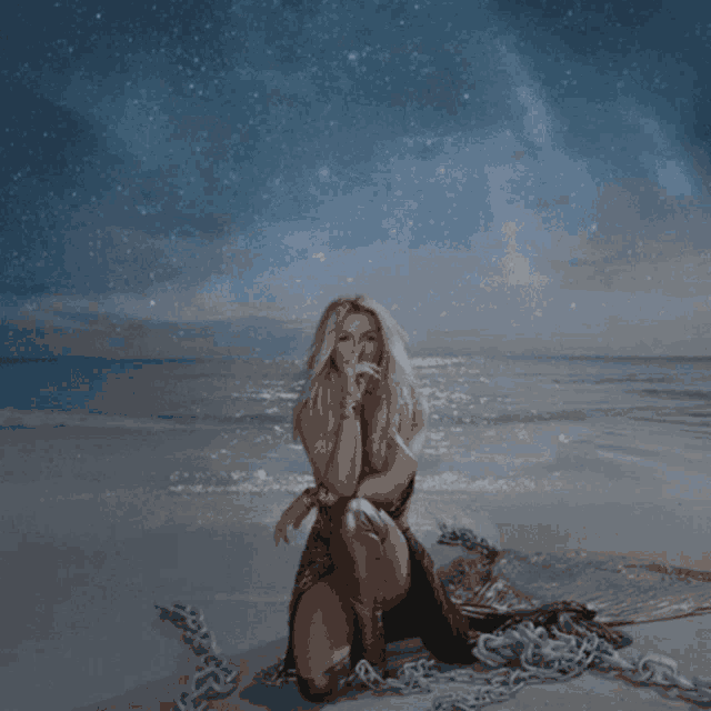 a woman is kneeling on a beach with chains around her