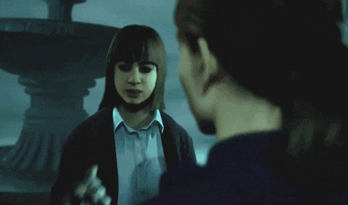 a woman in a black jacket is holding a man 's face in a dark room