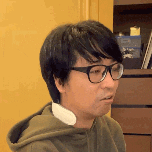 a man wearing glasses and a hooded sweatshirt has a white item around his neck