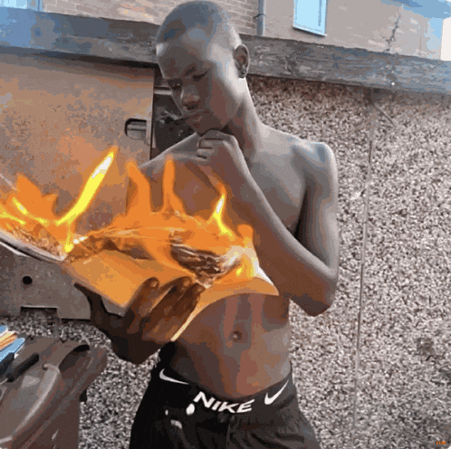 a shirtless man wearing nike shorts is holding a burning piece of paper