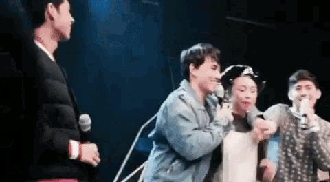 a group of people are standing on a stage with microphones in their hands .