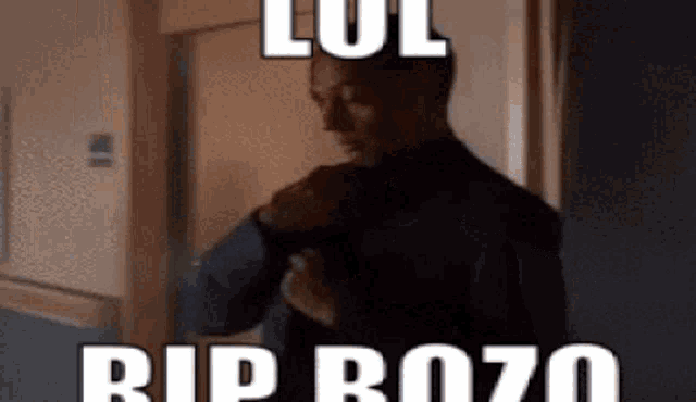 a man in a suit and tie is standing in a dark room with a meme on his face .