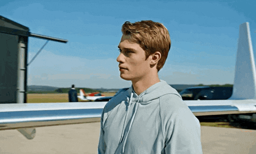 a man in a grey hoodie stands in front of a plane