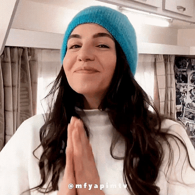 a woman wearing a blue beanie and a white sweater with her hands folded