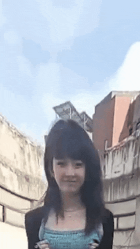 a young girl with long black hair is standing in front of a building and smiling .