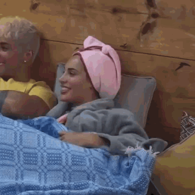 a woman with a towel wrapped around her head is laying on a bed next to another woman .