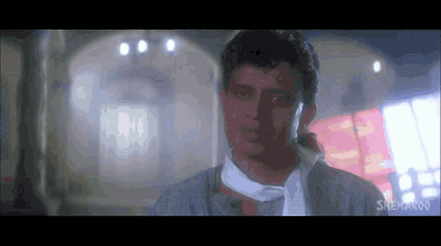 a man with a scarf around his neck is in a room with a sign that says sneha on it