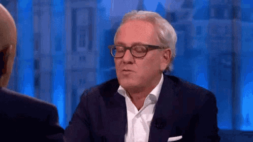 a man in a suit and glasses is talking to another man in a suit .