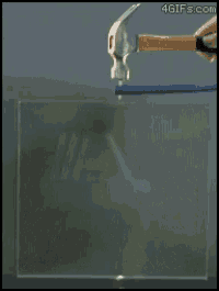a person is holding a hammer over a piece of glass with a green light coming out of it ..