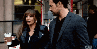 a man in a suit and a woman in a leather jacket are standing next to each other with the letters cw visible