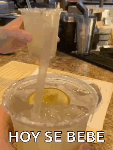 a margarita is being poured into a plastic cup with a straw and the words hoy se bebe on the bottom