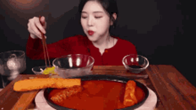 a woman is sitting at a table eating a plate of food with a spoon .