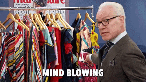a man in a suit is standing in front of a rack of clothes .