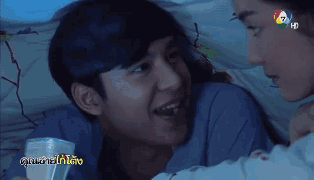 a man and a woman are laying on a bed with a tv screen behind them that says ' hk '