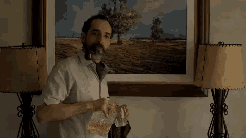 a man with a beard is smoking a cigar in front of a painting .