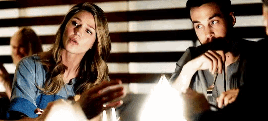 a man and a woman are sitting at a table talking to each other in a dark room .