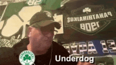 a man wearing a hat and ear buds is standing in front of a sign that says " underdog "