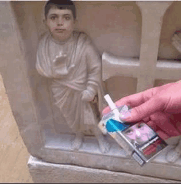 a person is holding a pack of cigarettes next to a statue of a boy .