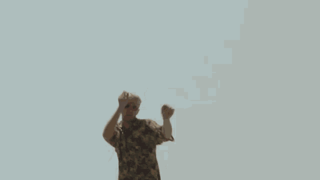 a man wearing sunglasses and a hawaiian shirt is dancing on the beach