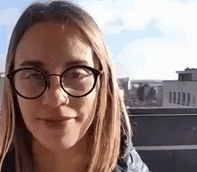 a woman wearing glasses is smiling for the camera in front of a building .